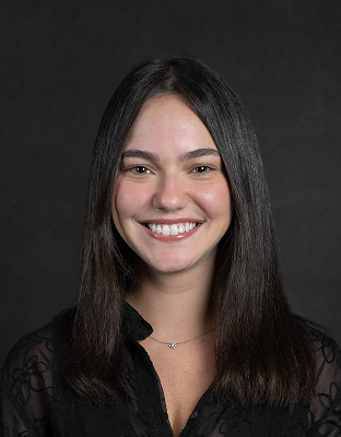 Anna King, with long dark hair, wearing a dark blouse, smiling broadly, looking at the camera.