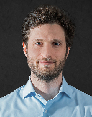Daniel Epstein, man with dark curly hair, beard, light blue dress shirt, smiling, looking forward.