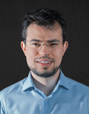 Kauê Silva, man with short dark hair, beard, glasses, light blue dress shirt, smiling, looking forward.