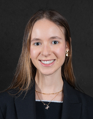 Marlyn Picciotto, smiling, with long light-colored hair, gold earrings, and dark blazer.