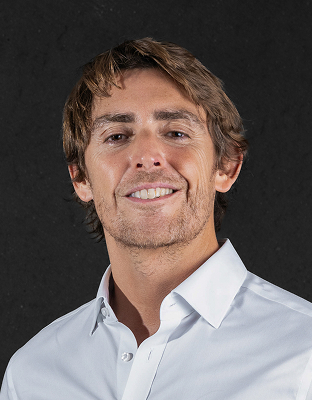 Michael Timmermann, man with medium wavy light brown hair, light dress shirt, smiling, looking forward.