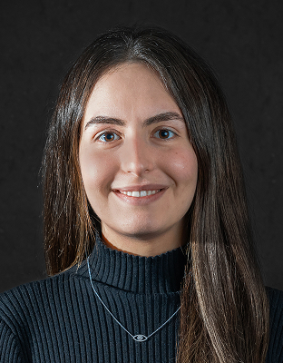 Vanessa Dayan, smiling, with long dark hair, wearing a black turtleneck top.